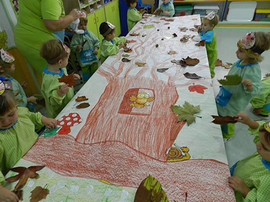 Un grupo de niños está sentado alrededor de una mesa con un dibujo de un árbol en ella.