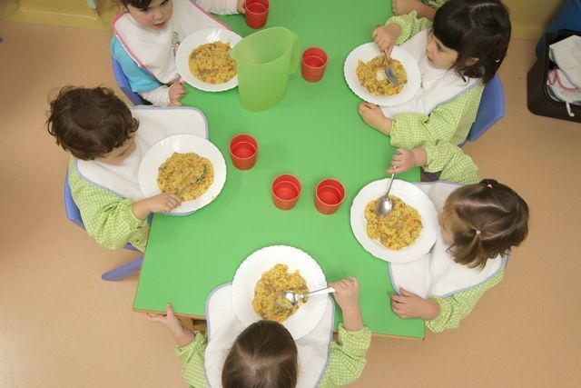 Un grupo de niños está sentado en una mesa comiendo cereal.
