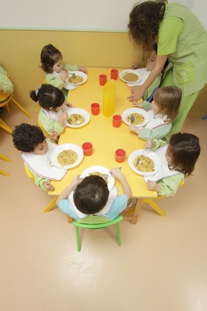 Un grupo de niños están sentados alrededor de una mesa comiendo comida.