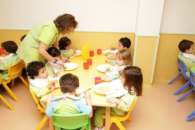 Un grupo de niños están sentados alrededor de una mesa comiendo comida.