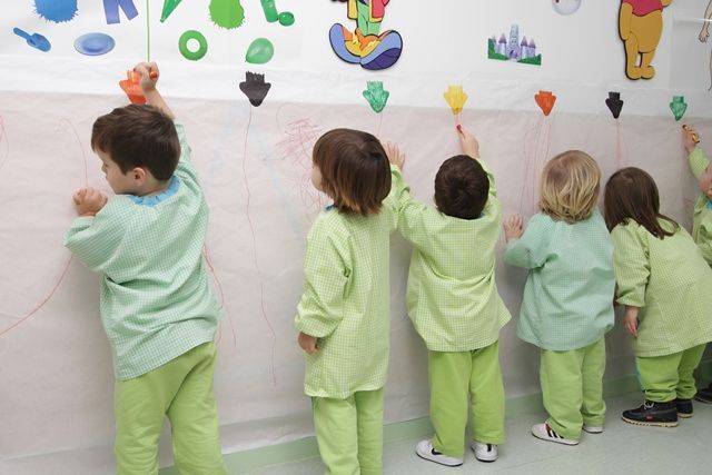 Un grupo de niños con monos verdes dibujan en una pared.