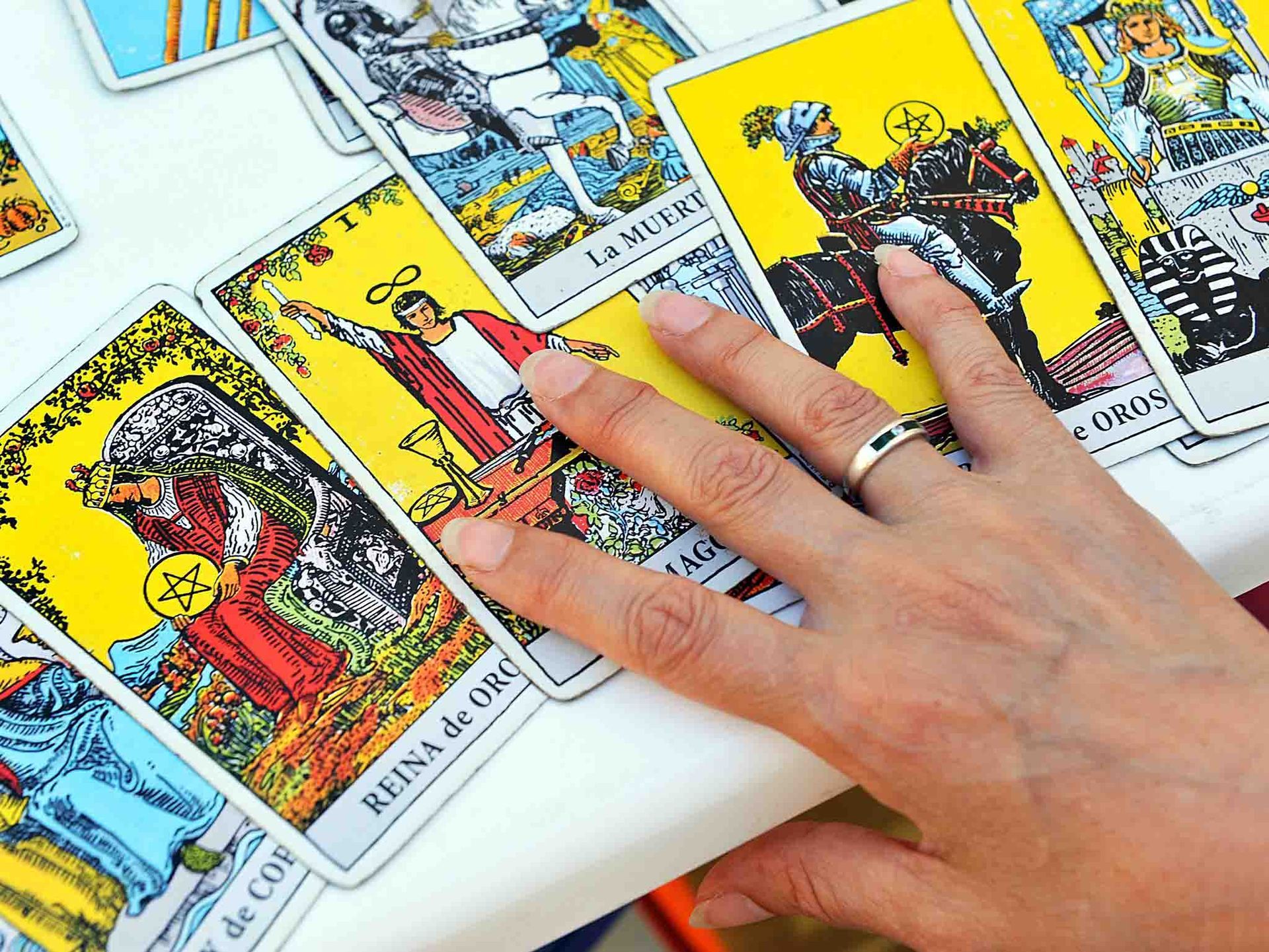 La mano de una mujer se extiende hacia una carta del tarot que dice 'Reina de Oro'.