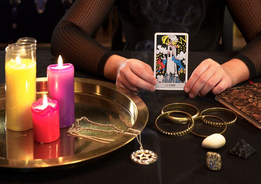 Una mujer está sentada en una mesa con velas y una carta del tarot.