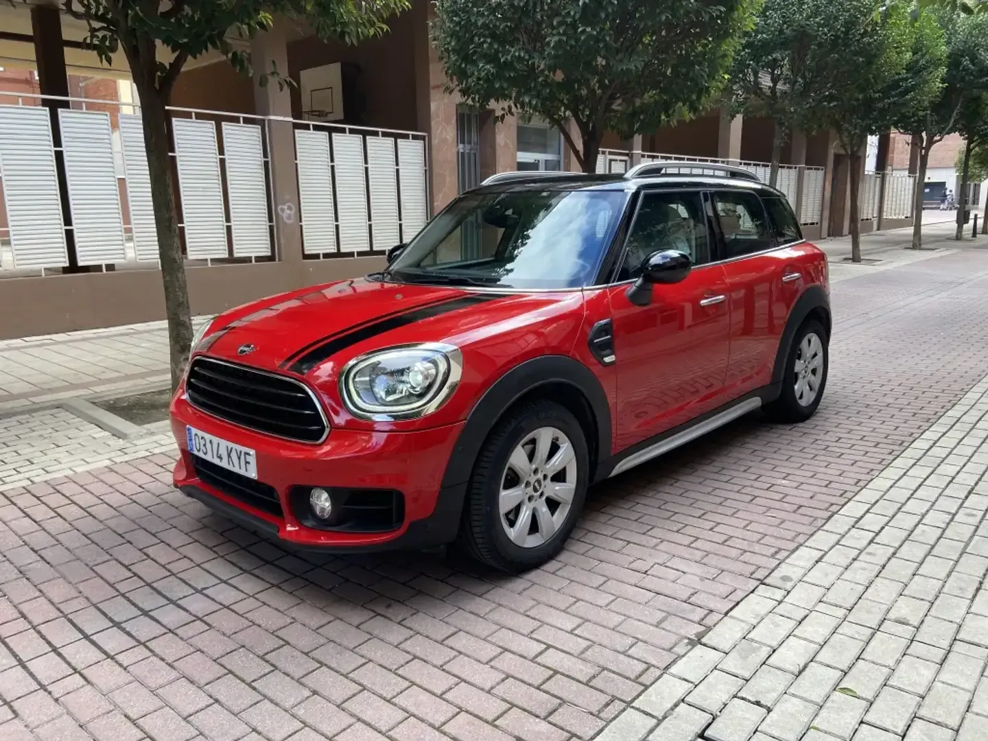 Un Mini Cooper Countryman rojo está estacionado en una acera de ladrillos.