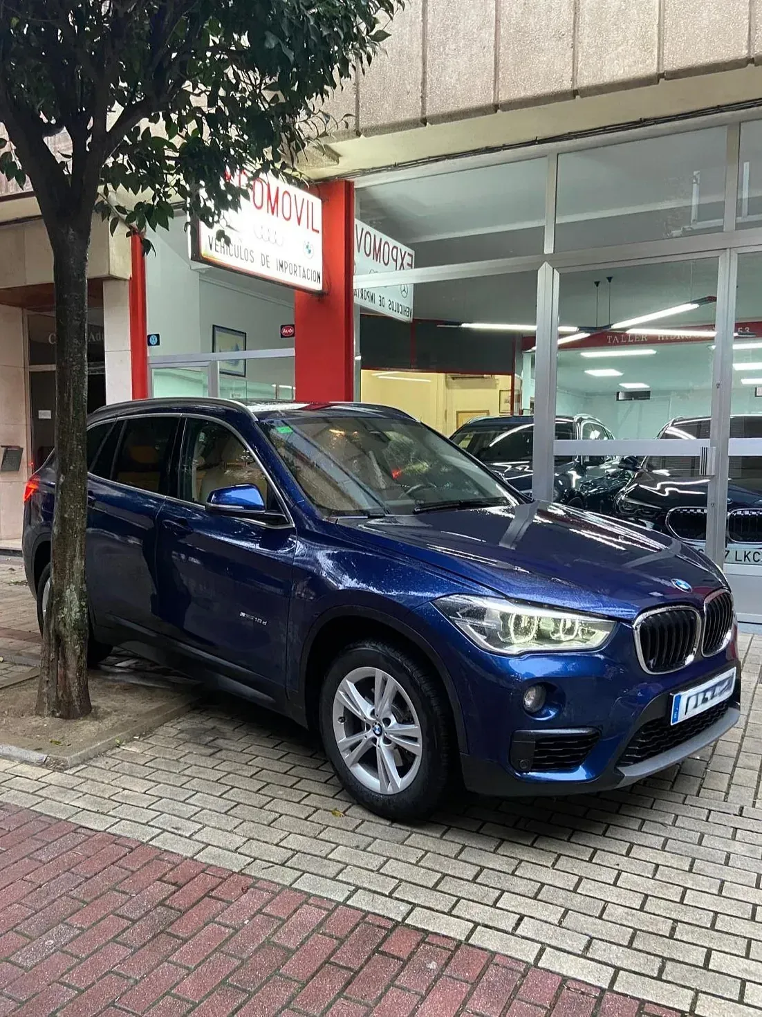 Un BMW X1 azul está estacionado frente a un concesionario de automóviles.