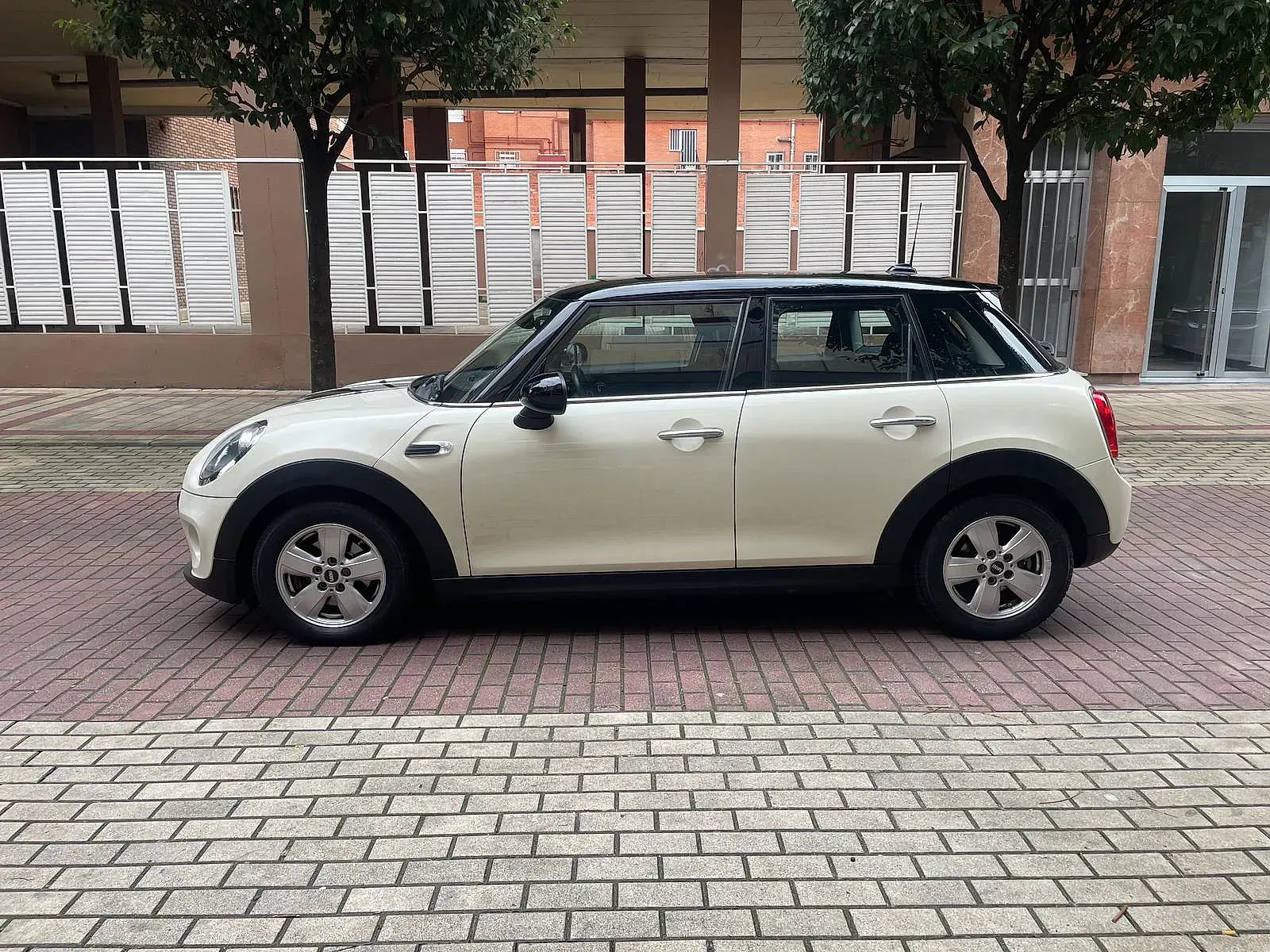 Un Mini Cooper blanco está estacionado en una acera de ladrillos.