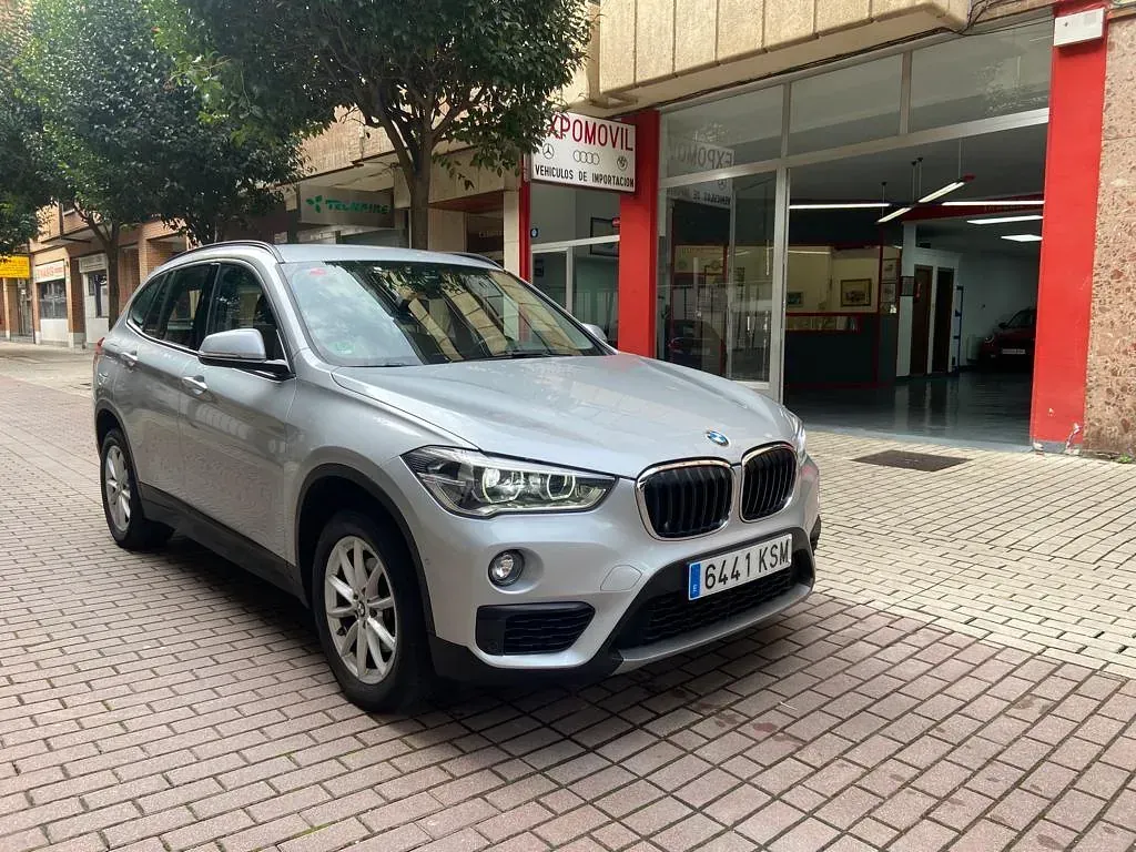 Un BMW X1 plateado está estacionado frente a un concesionario de automóviles.