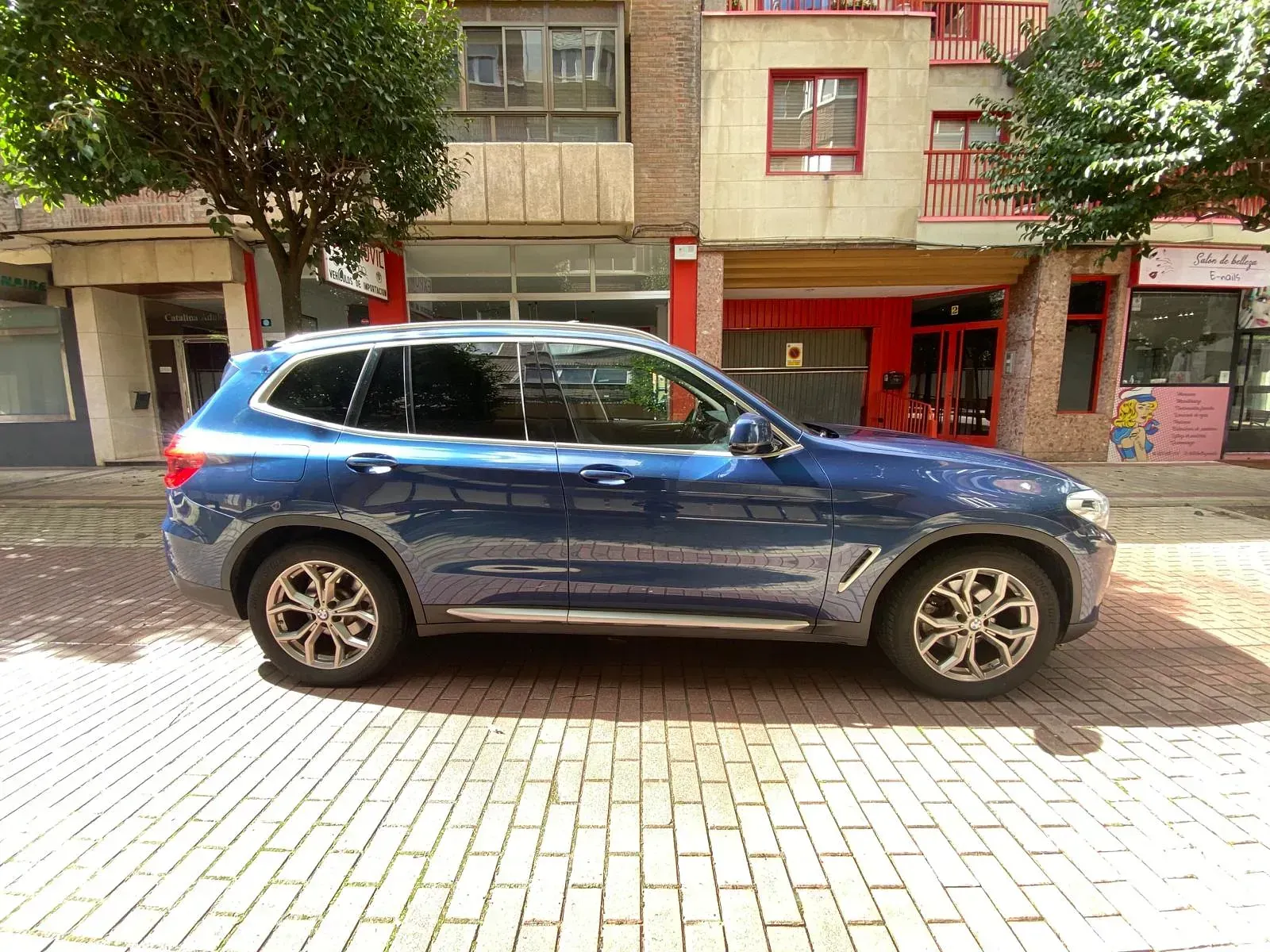 Una camioneta azul está estacionada en una acera de ladrillos frente a un edificio.