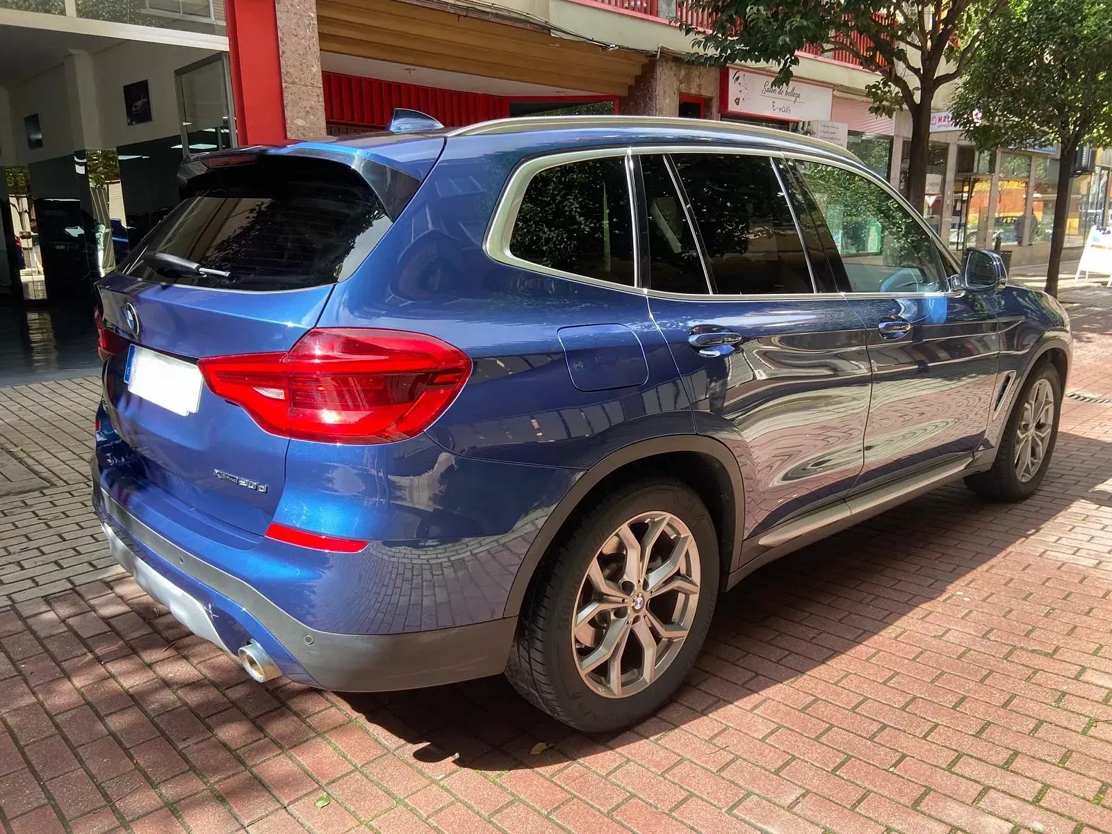 Un BMW X3 azul está estacionado en una acera de ladrillos frente a un edificio.