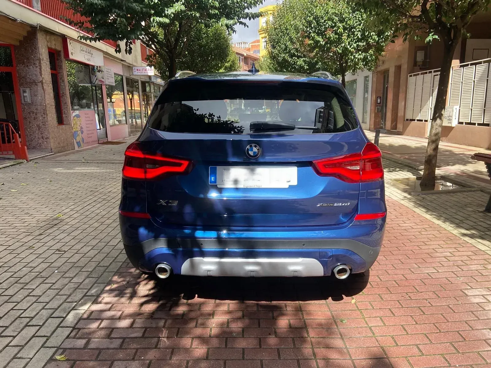 Un BMW X3 azul está estacionado en una acera de ladrillos.