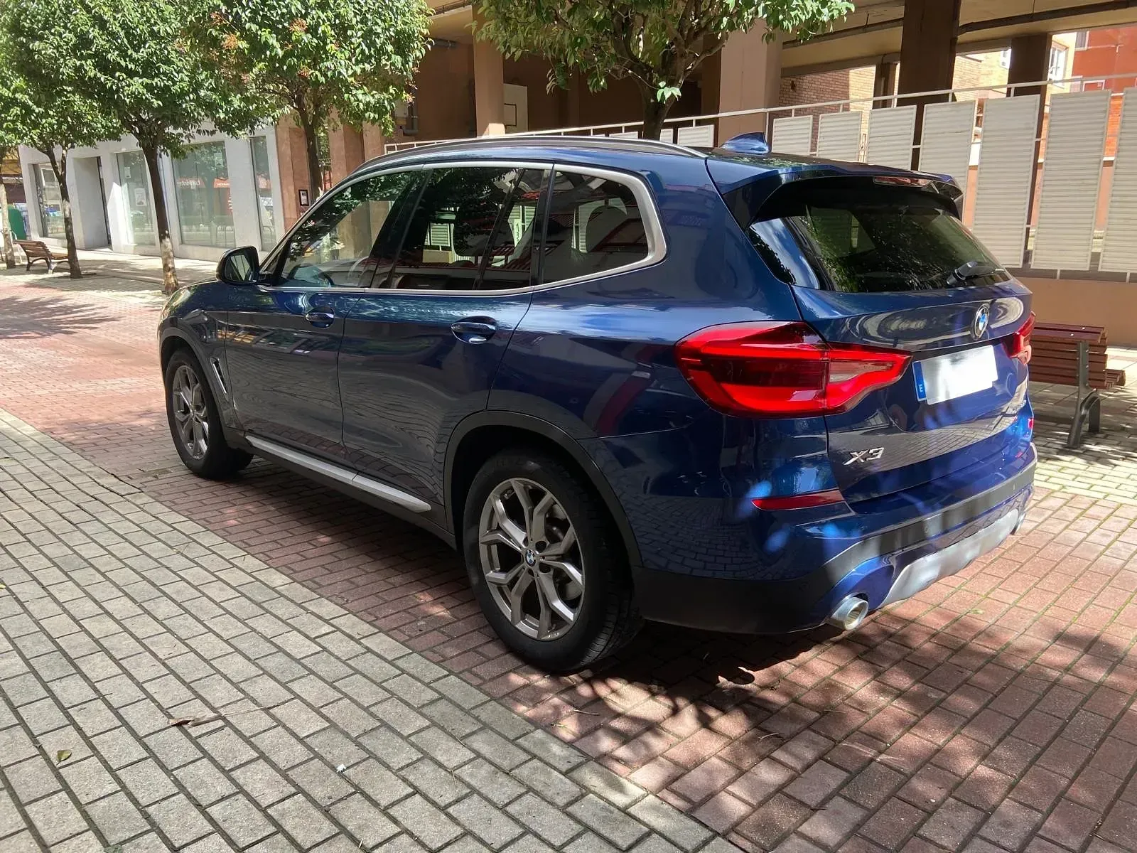 Un BMW X3 azul está estacionado en una acera de ladrillos.