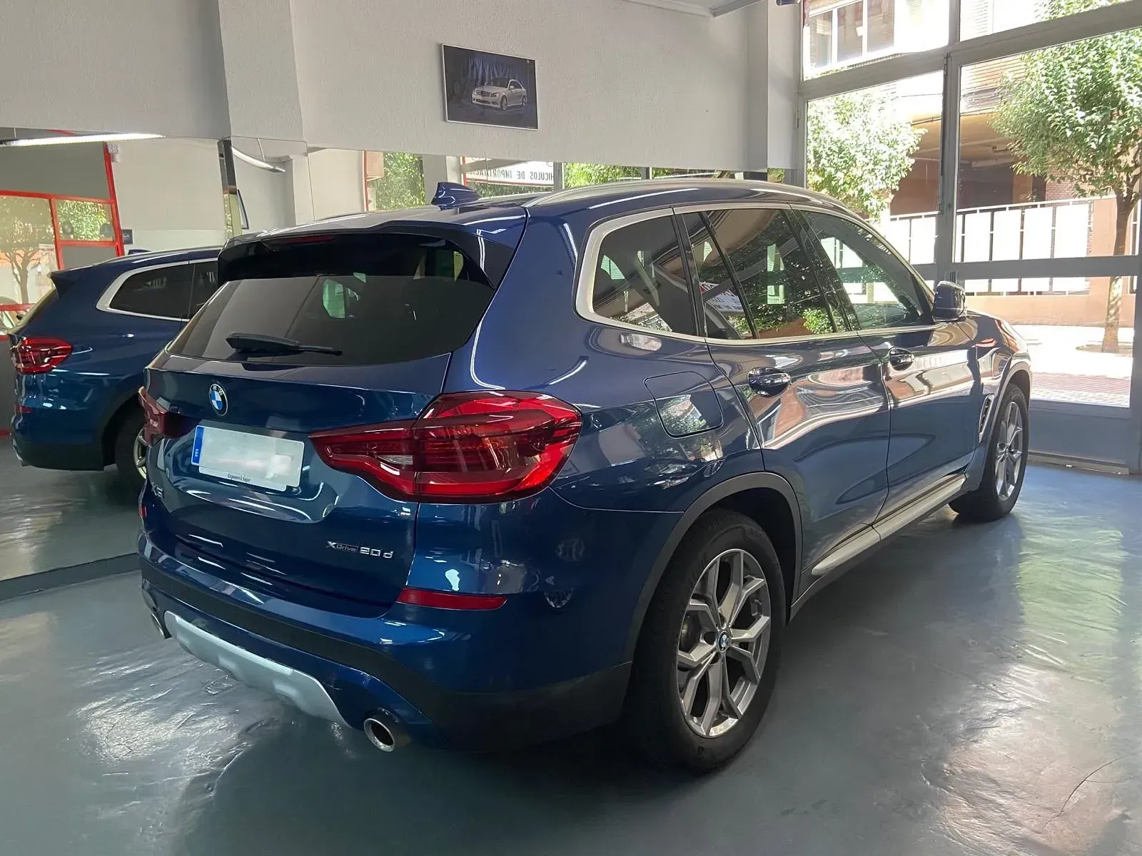 Un BMW X3 azul está estacionado en una sala de exposición.