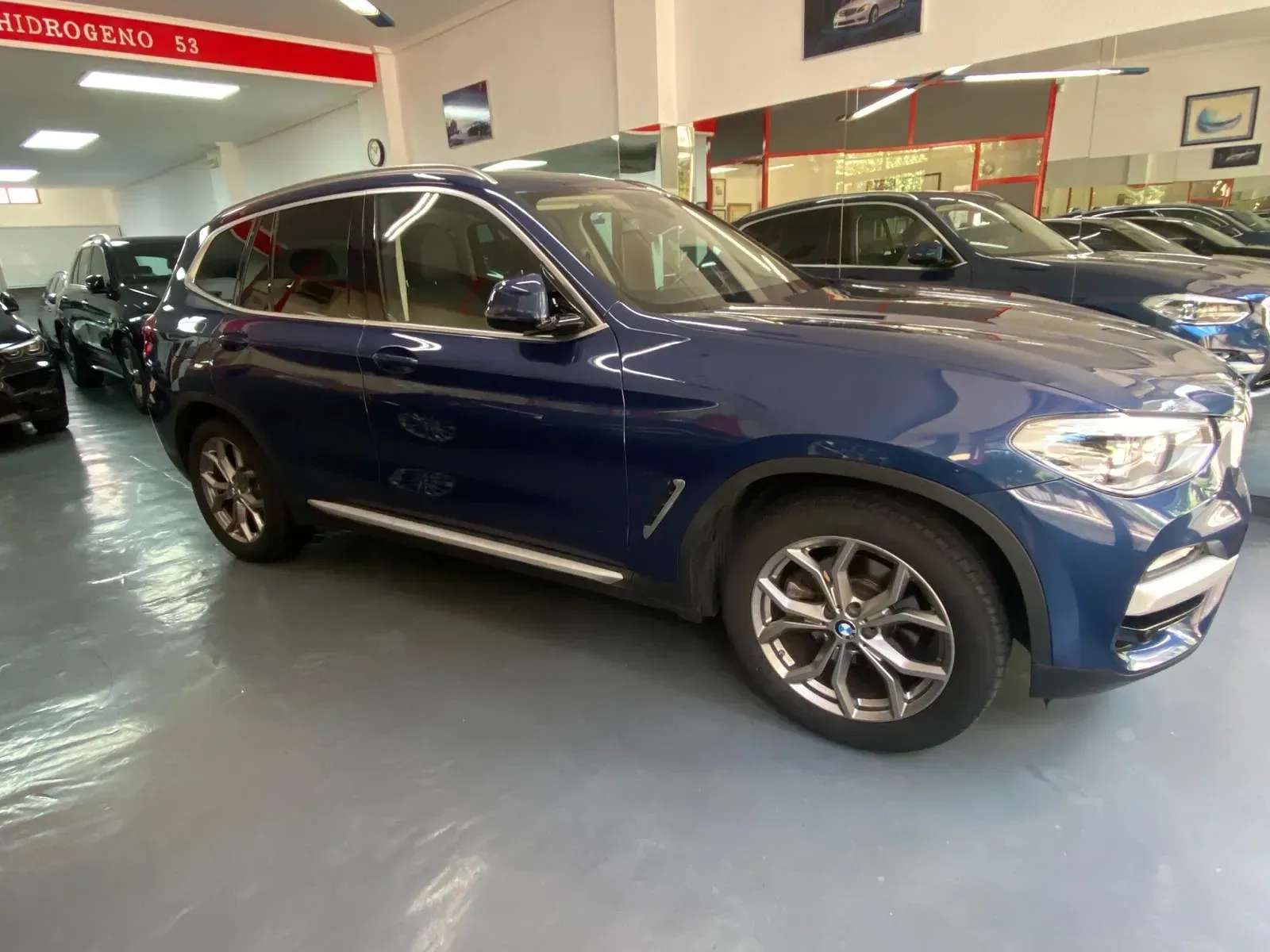 Un BMW X3 azul está estacionado en una sala de exposición.