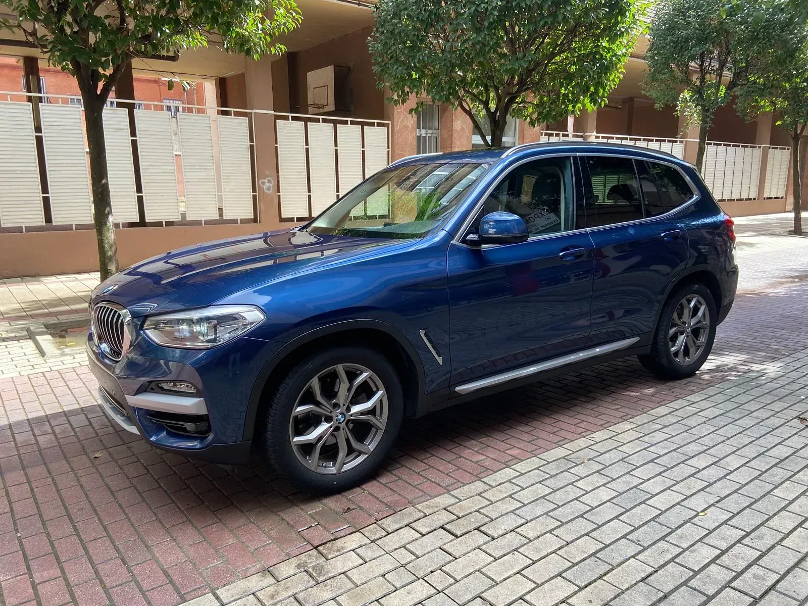 Un BMW X3 azul está estacionado en una acera de ladrillos.