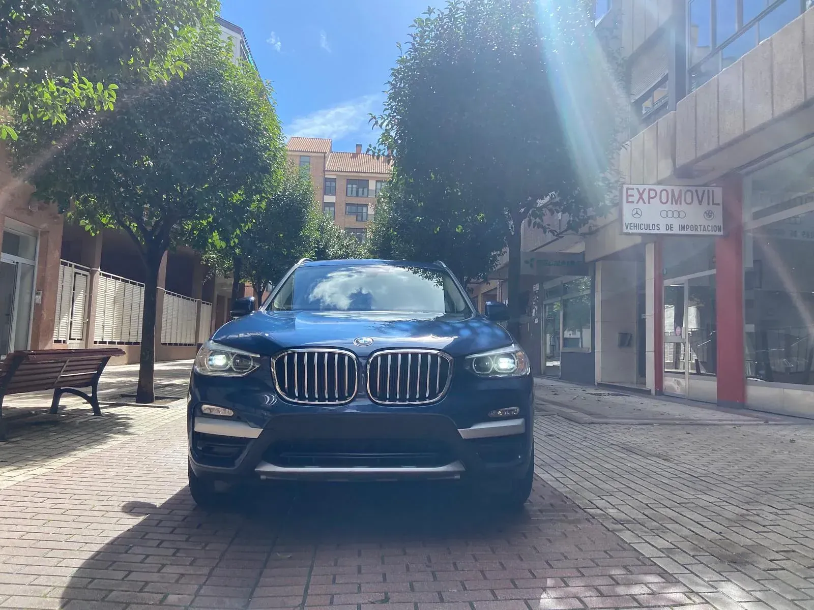 Un BMW X3 azul está estacionado en una acera de ladrillos frente a un edificio.