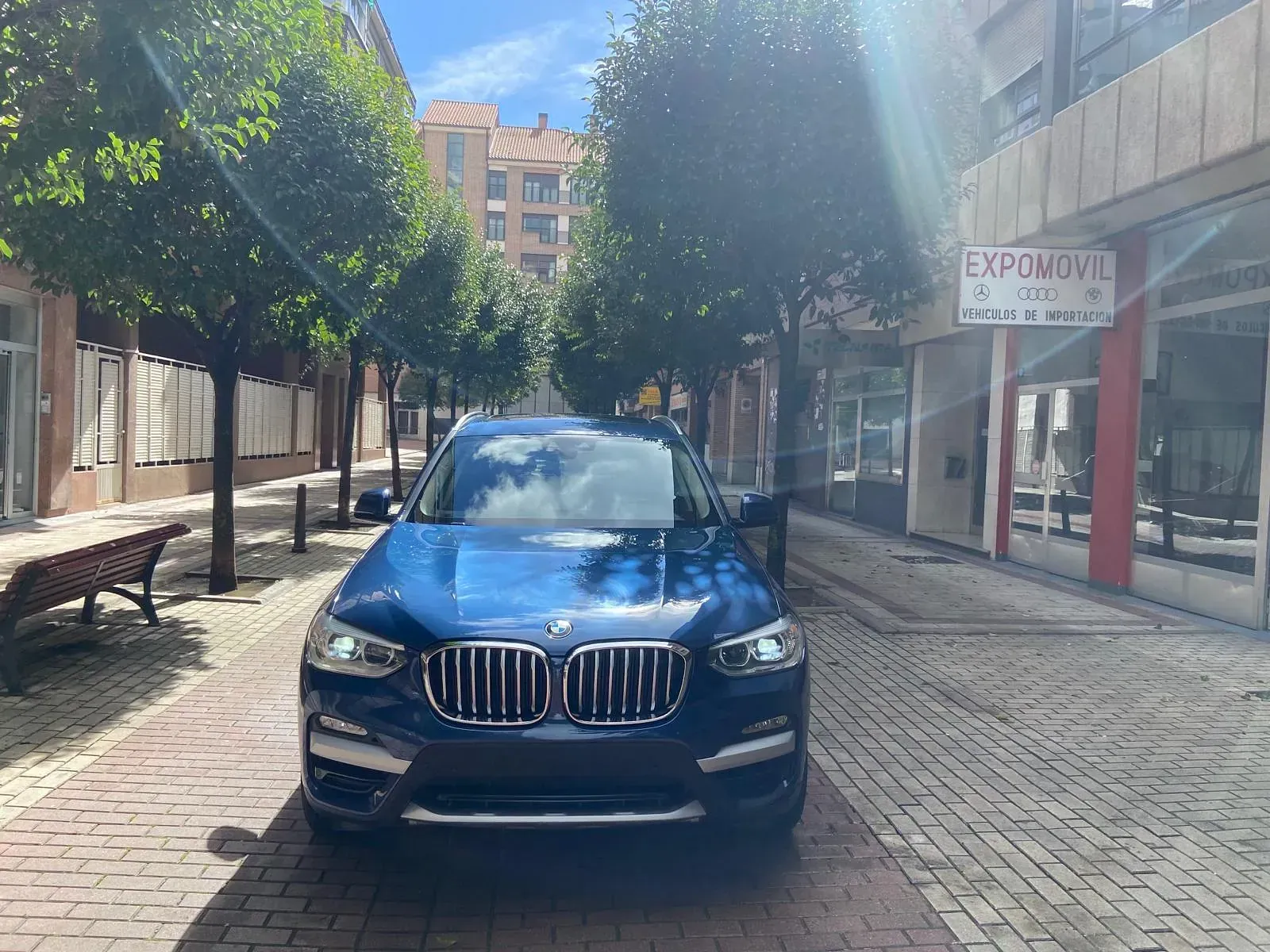 Un BMW azul está estacionado en una acera de ladrillos frente a un edificio.