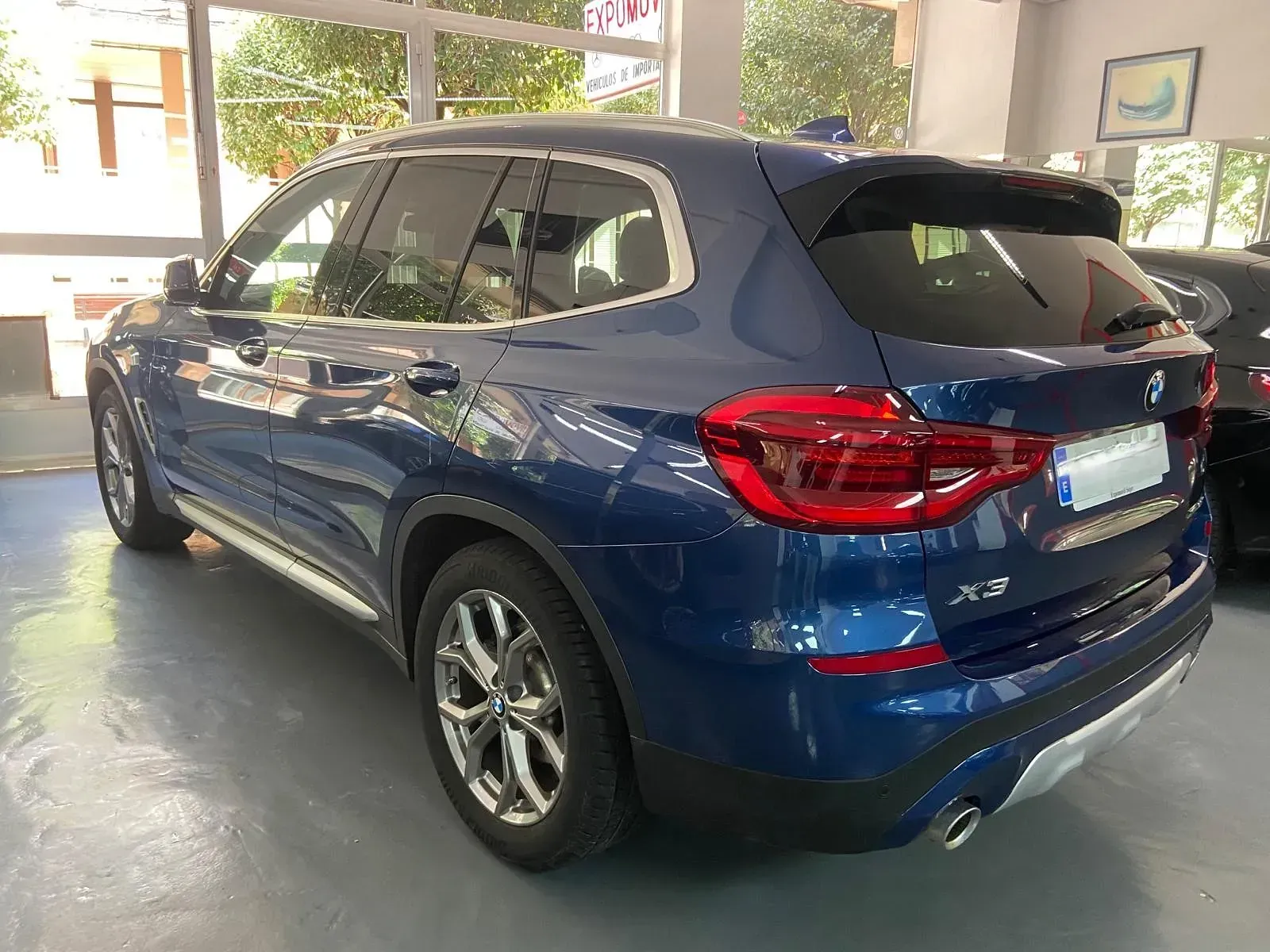 Un BMW X3 azul está estacionado en una sala de exposición.