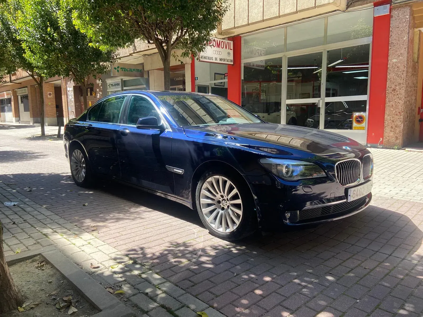 Un BMW azul está estacionado en una acera de ladrillos frente a un edificio.