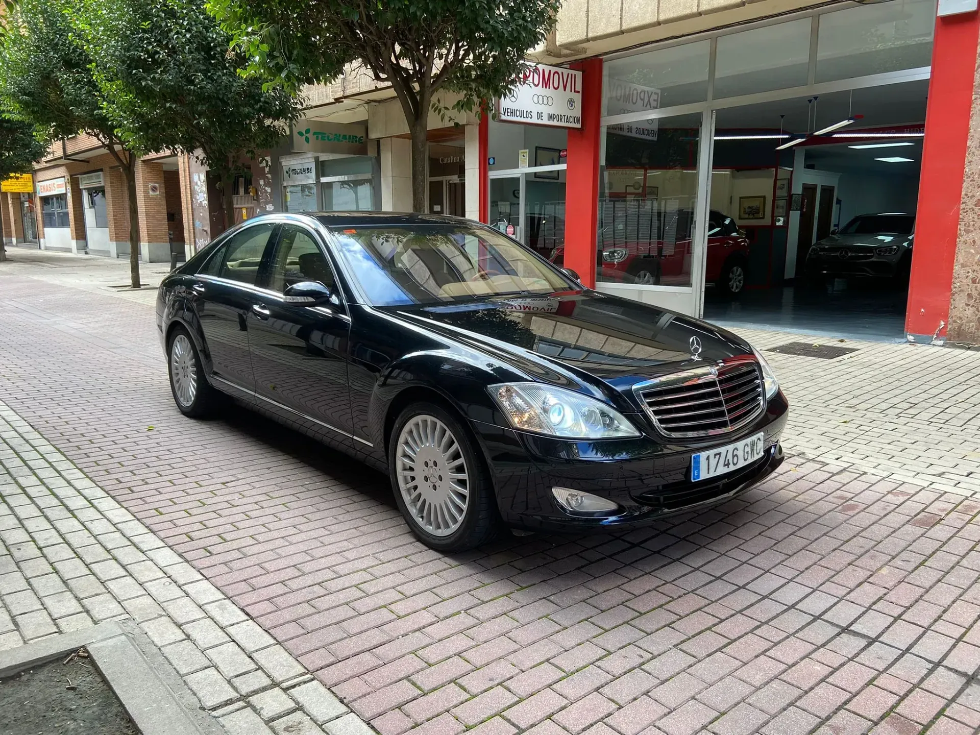 Un coche negro está estacionado en una acera de ladrillos frente a un concesionario de automóviles.