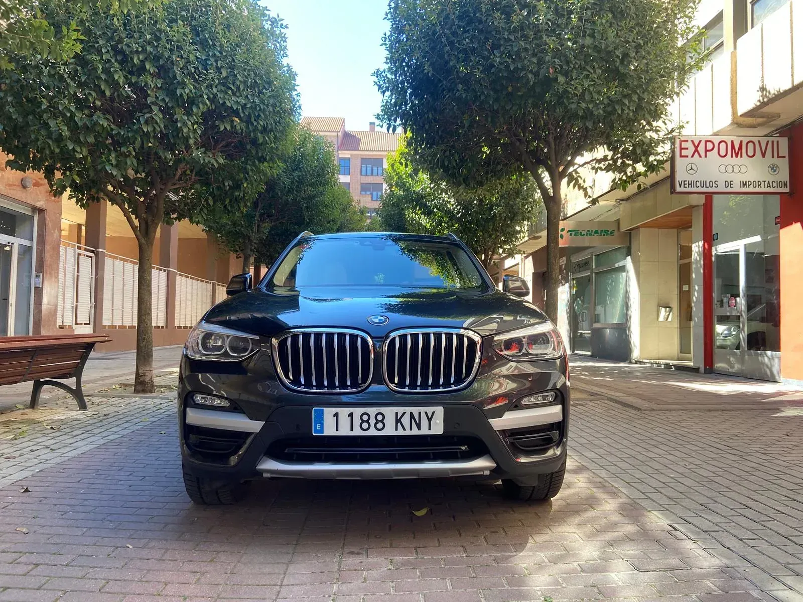Un BMW negro está estacionado en una acera de ladrillos frente a un edificio.