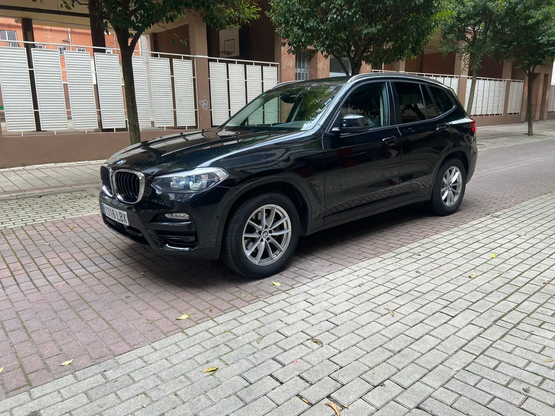 Un BMW X3 negro está estacionado en una acera de ladrillos.