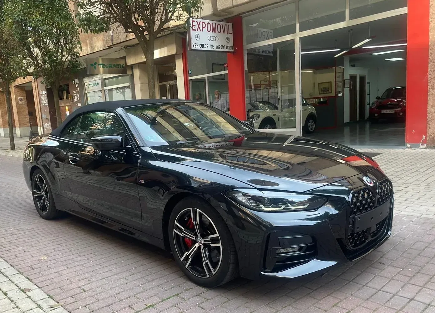 Un convertible negro está estacionado frente a un concesionario de automóviles.