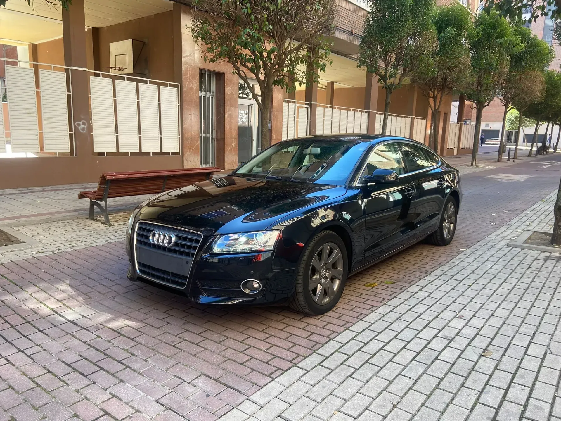 Un coche negro está estacionado en una acera de ladrillos frente a un edificio.