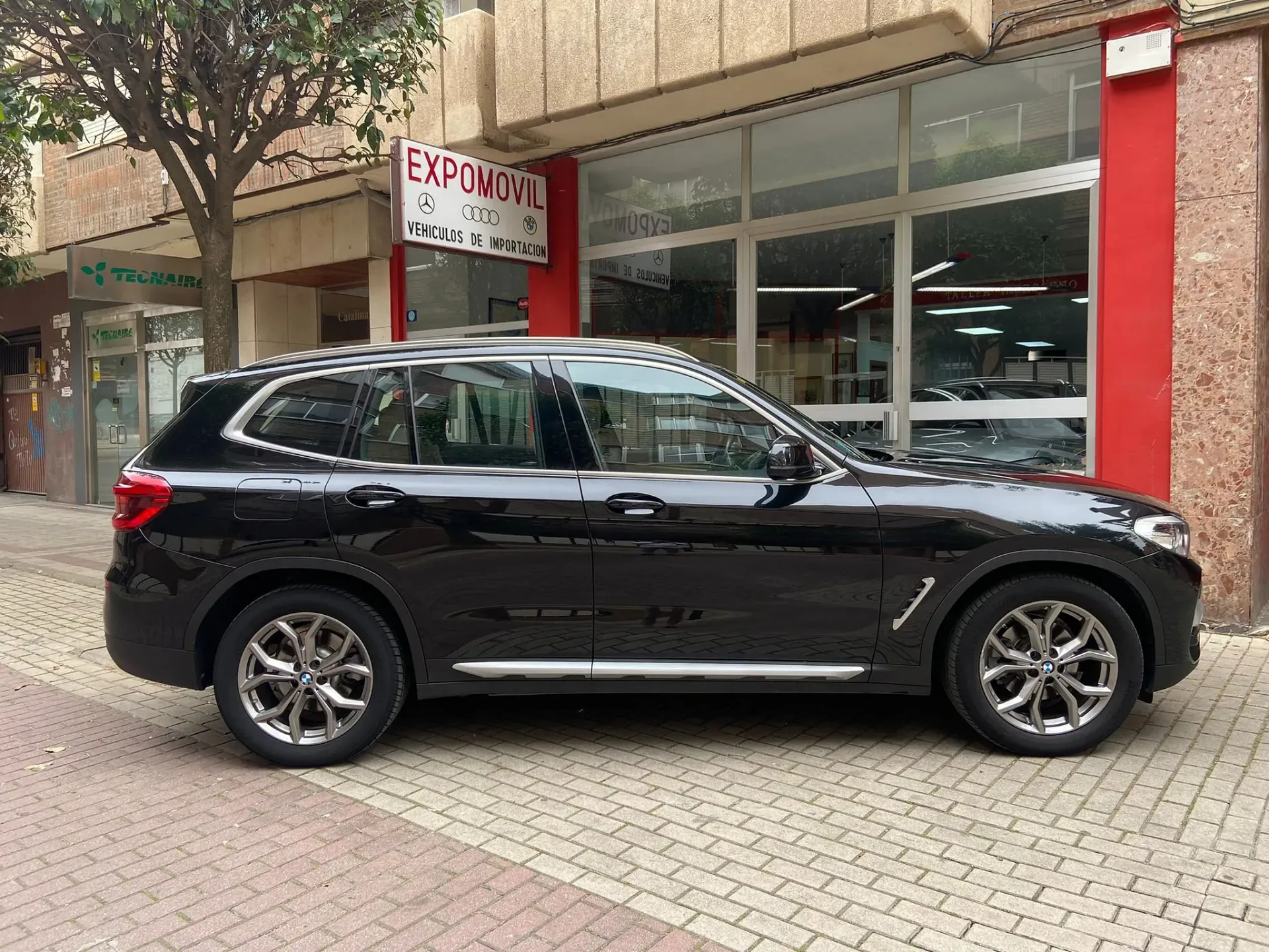 Un BMW X3 negro está estacionado frente a un concesionario de automóviles.