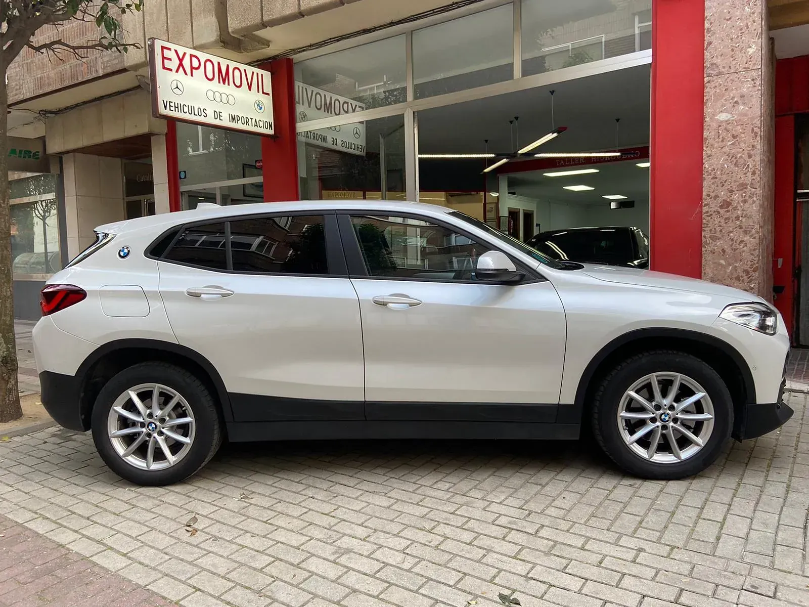 Un BMW X2 blanco está estacionado frente a un concesionario de automóviles.