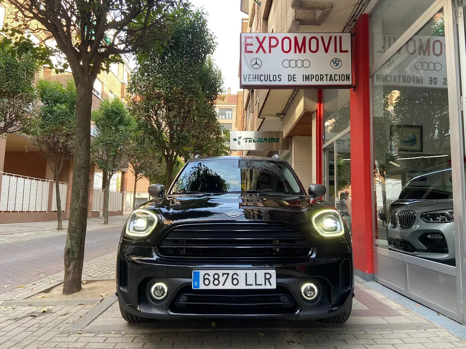Un Mini Cooper negro está estacionado frente a un concesionario de automóviles.