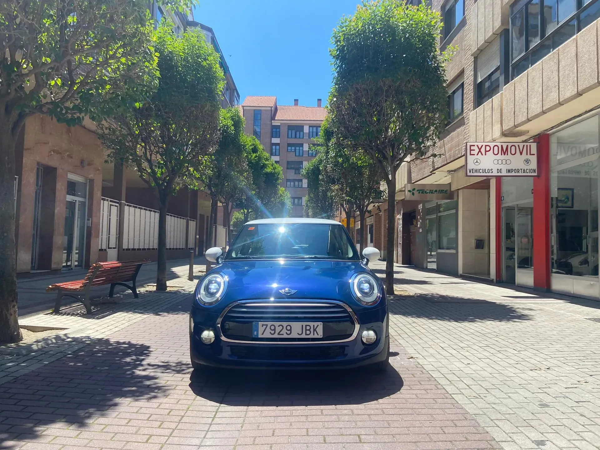 Un Mini Cooper azul está estacionado en una acera de ladrillos en una ciudad.