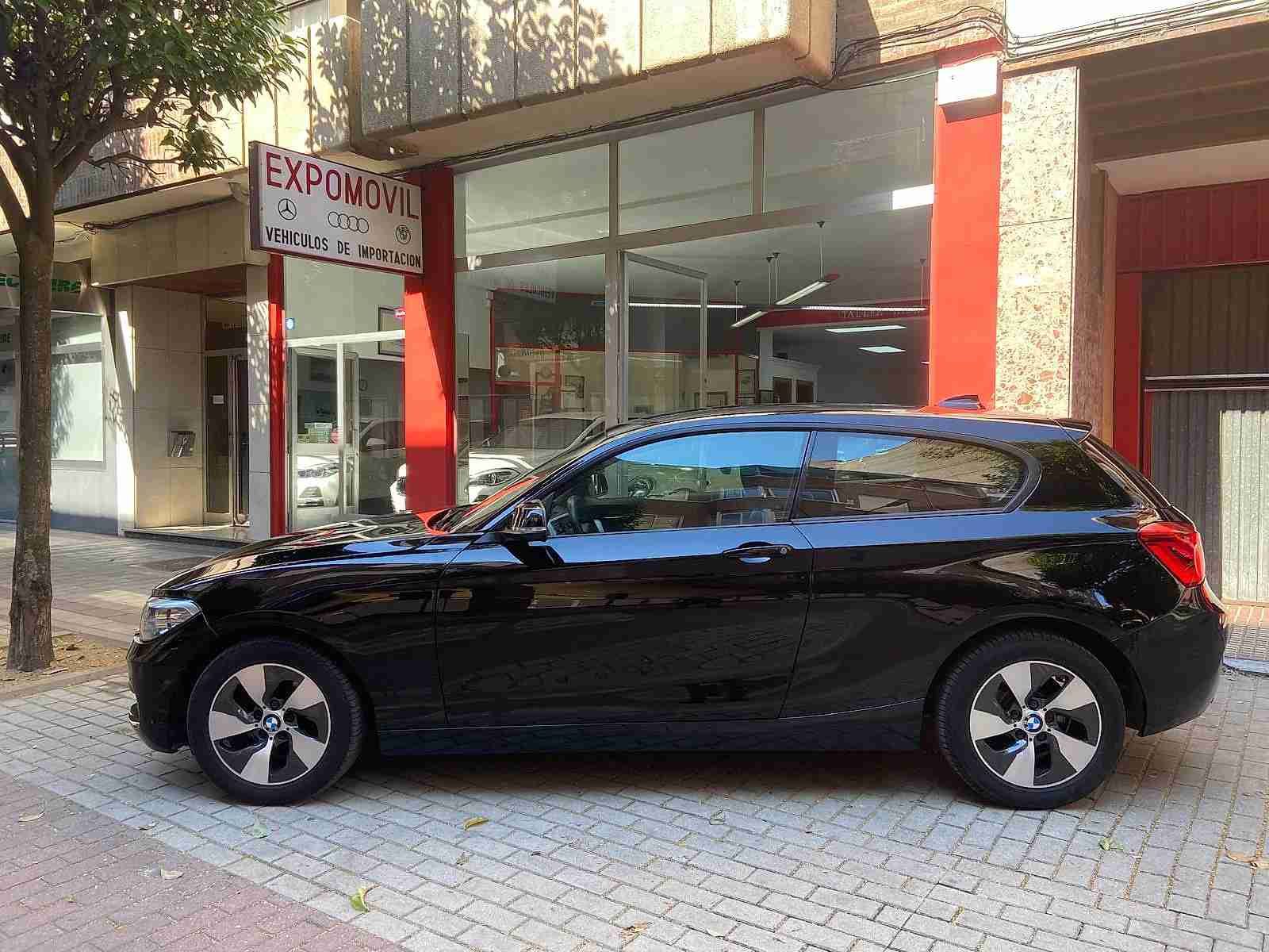 Un coche negro está aparcado delante de un concesionario de automóviles.
