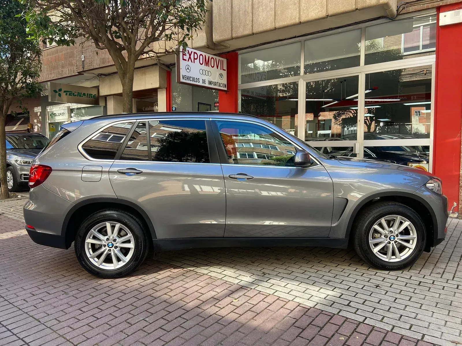 Un BMW X5 está estacionado frente a un concesionario de automóviles.