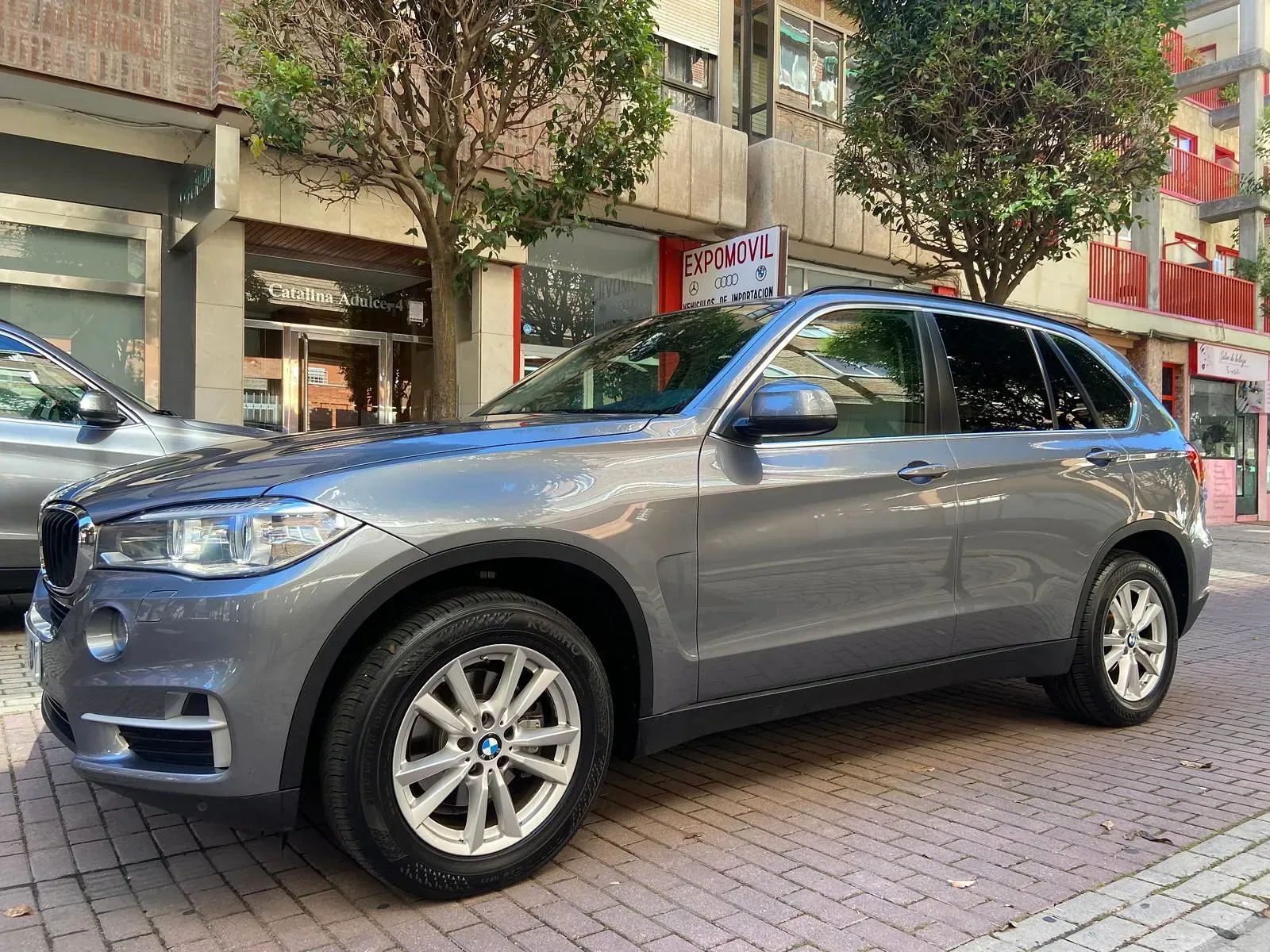 Un BMW X5 está estacionado en una acera de ladrillos frente a un edificio.