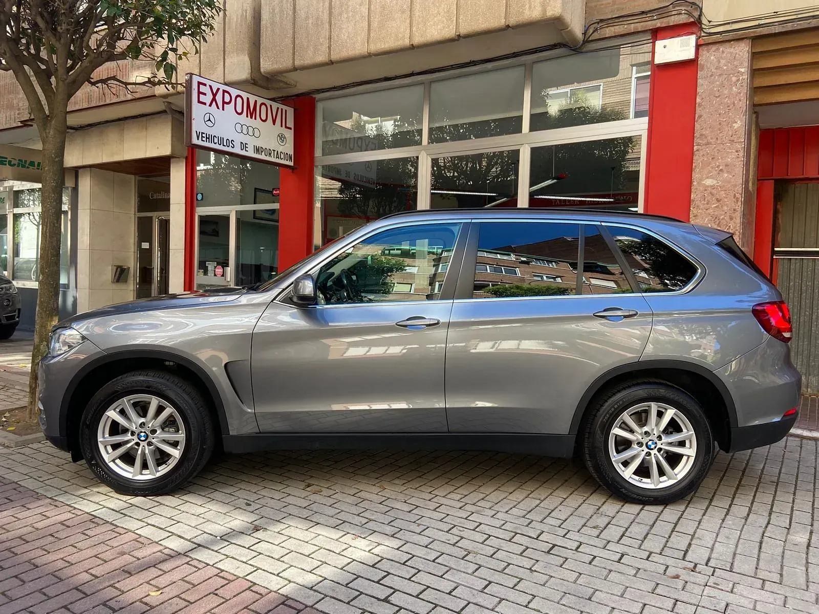 Un BMW X5 está estacionado frente a un concesionario de automóviles.