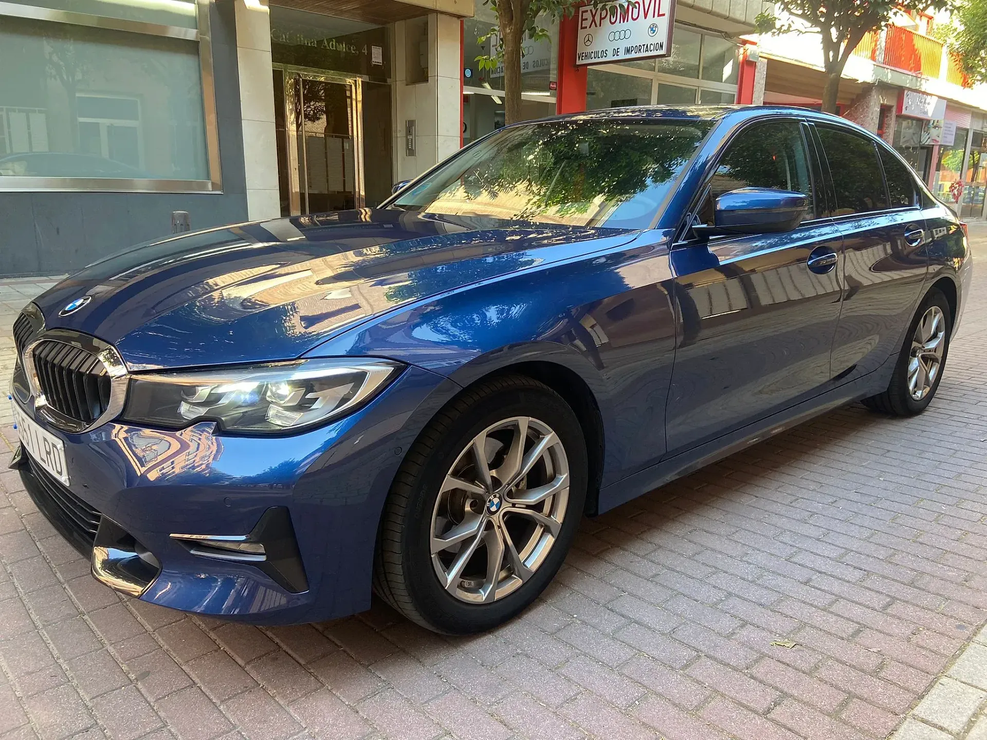 Un BMW Serie 3 azul está estacionado en una acera frente a un edificio.