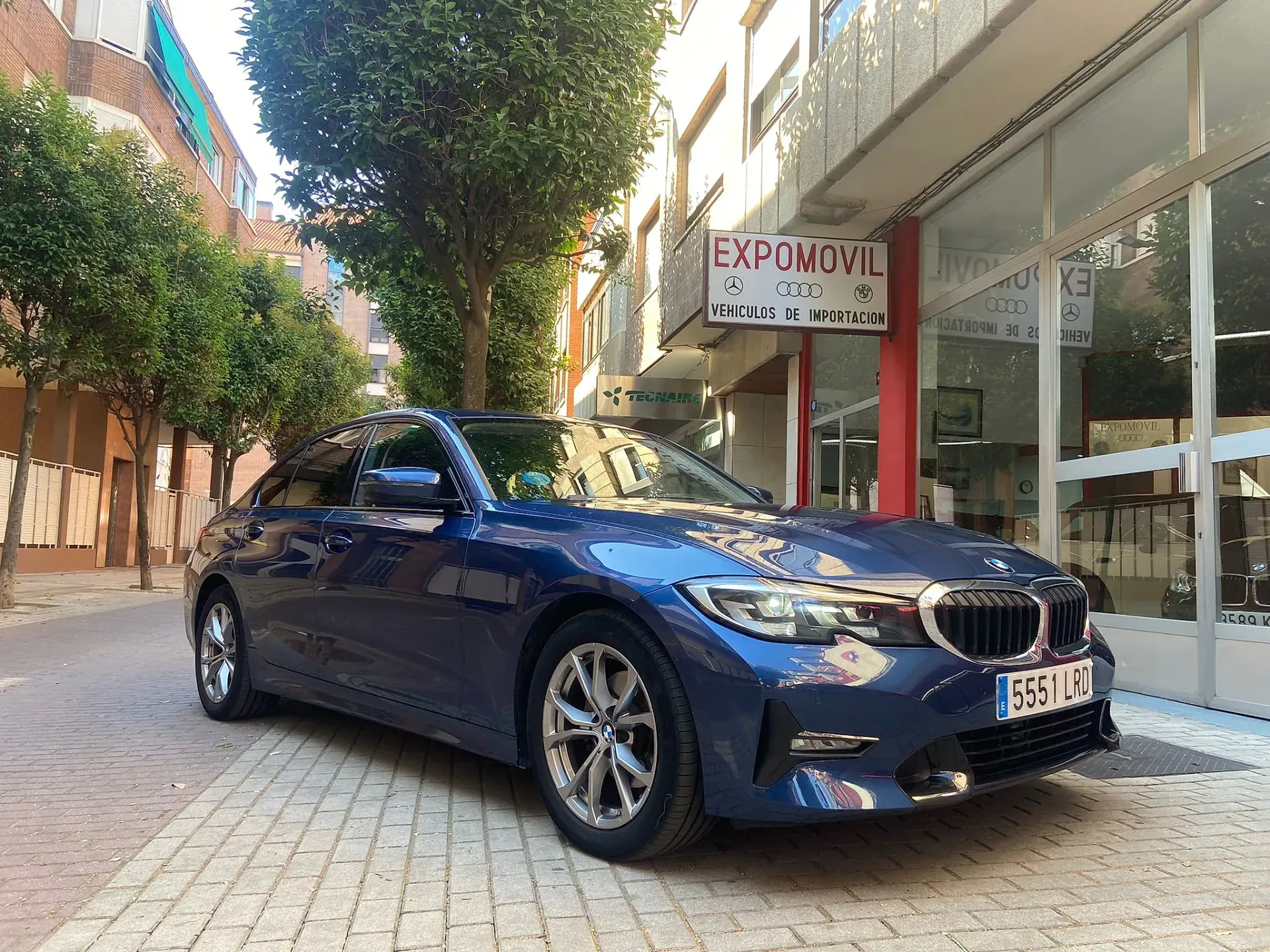 Un BMW Serie 3 azul está estacionado frente a un edificio.
