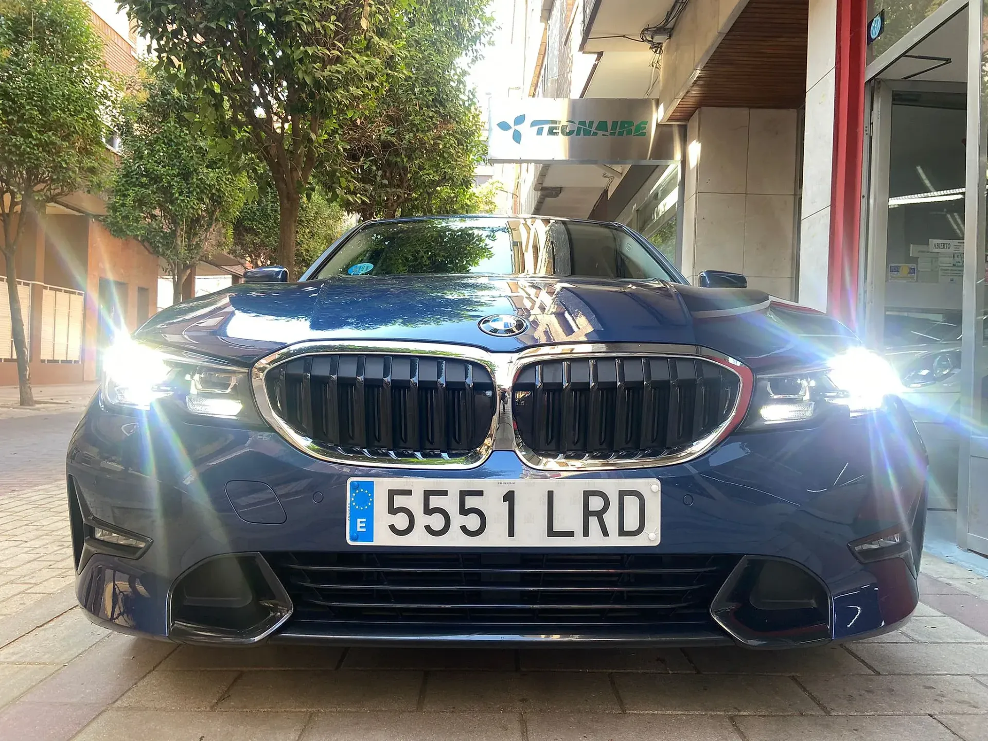 Un BMW azul está estacionado al costado de la carretera frente a un edificio.
