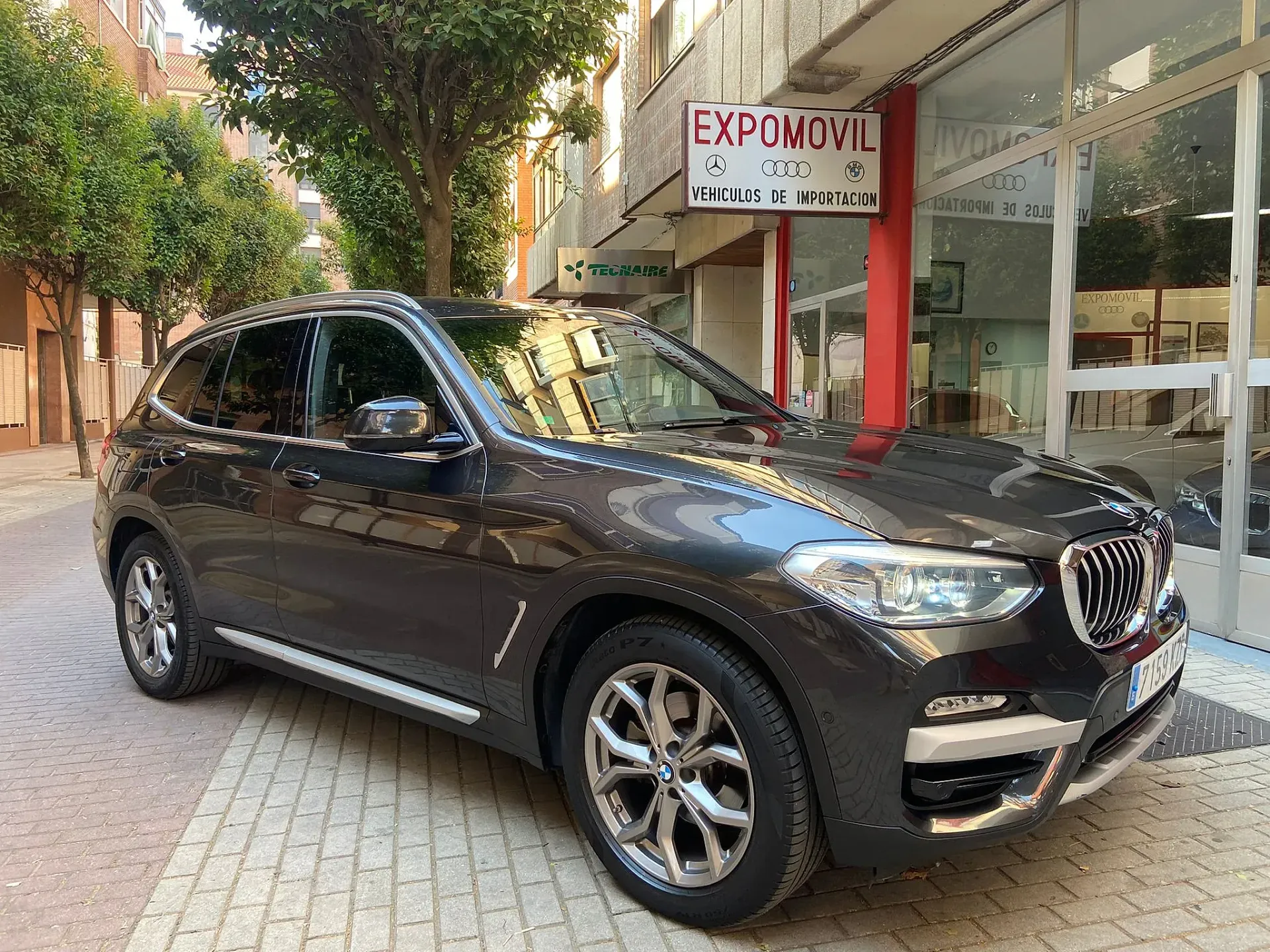 Un BMW X3 negro está estacionado frente a un concesionario de automóviles.