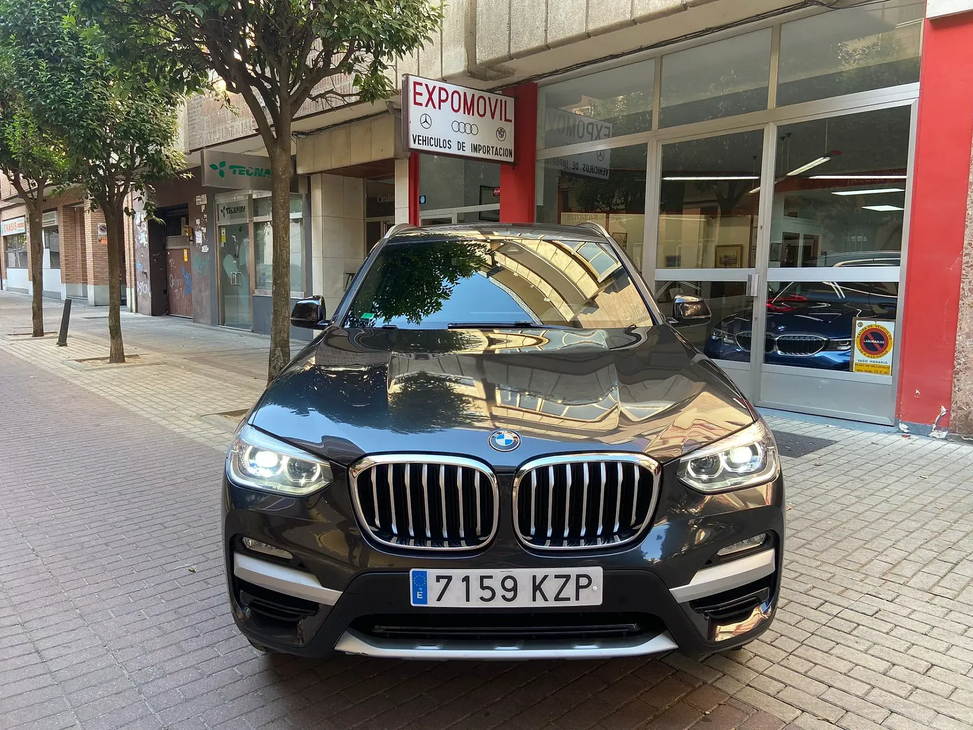 Un BMW X3 negro está estacionado en una acera de ladrillos frente a un edificio.