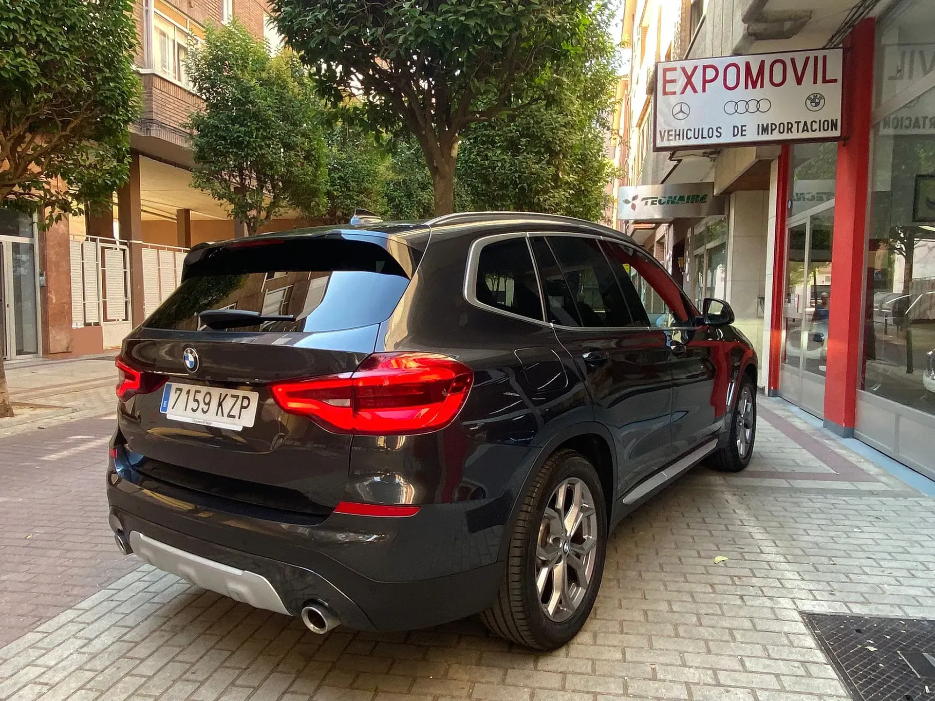 Un BMW X3 negro está estacionado en una acera de ladrillos frente a un edificio.