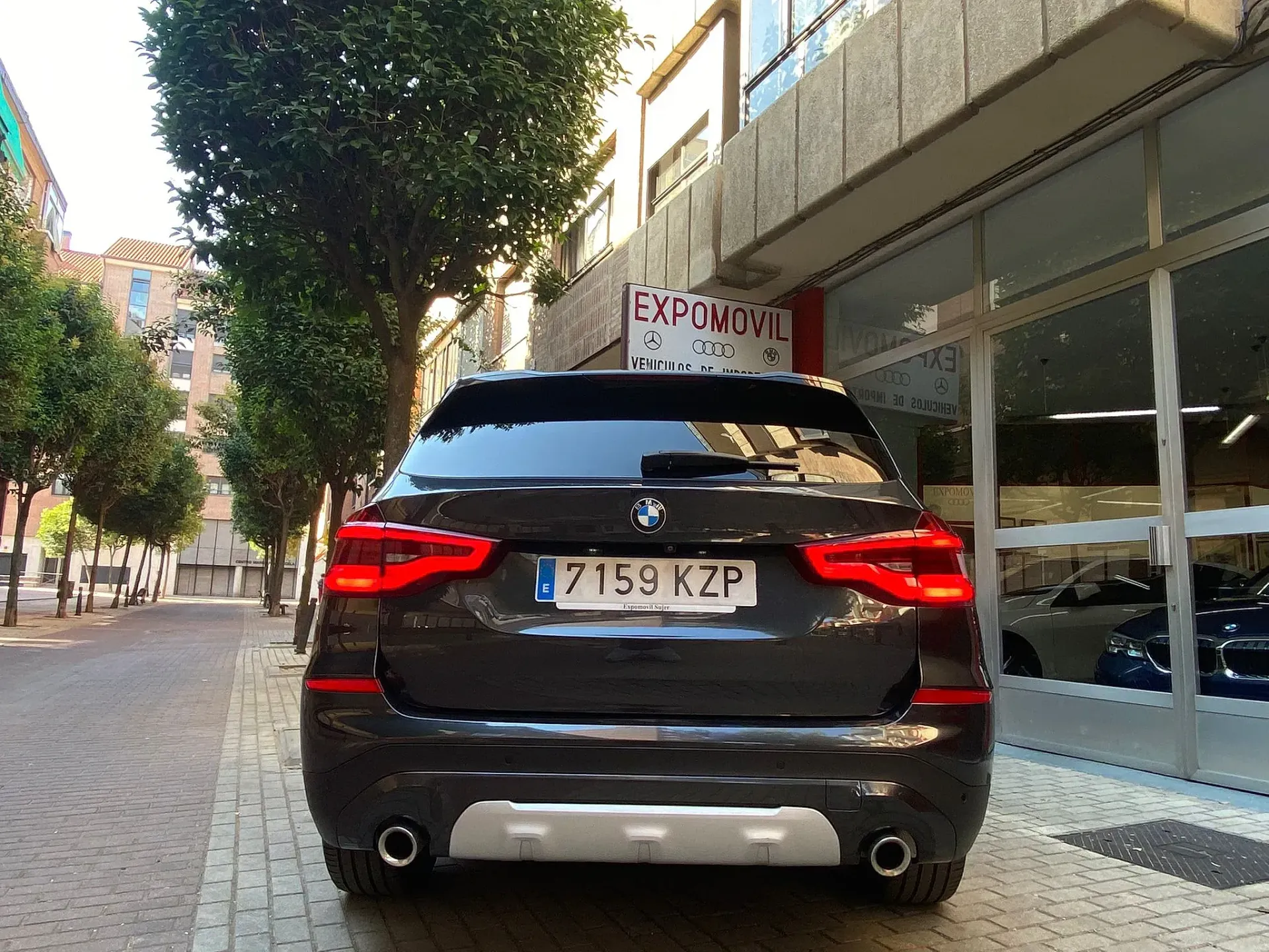 Un BMW X3 negro está estacionado frente a un concesionario de automóviles.