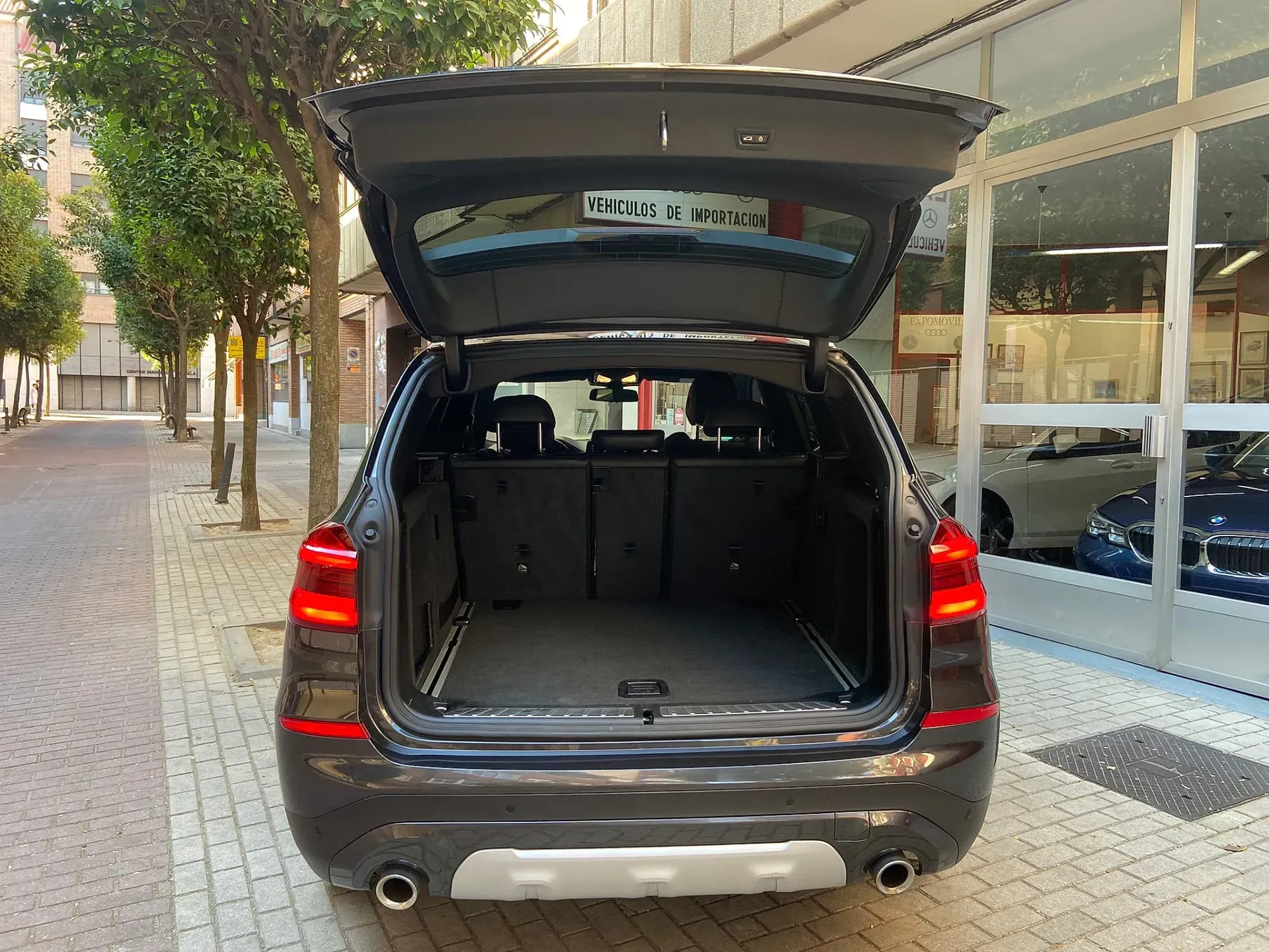 La parte trasera de un coche con el maletero abierto está aparcada al costado de la carretera.