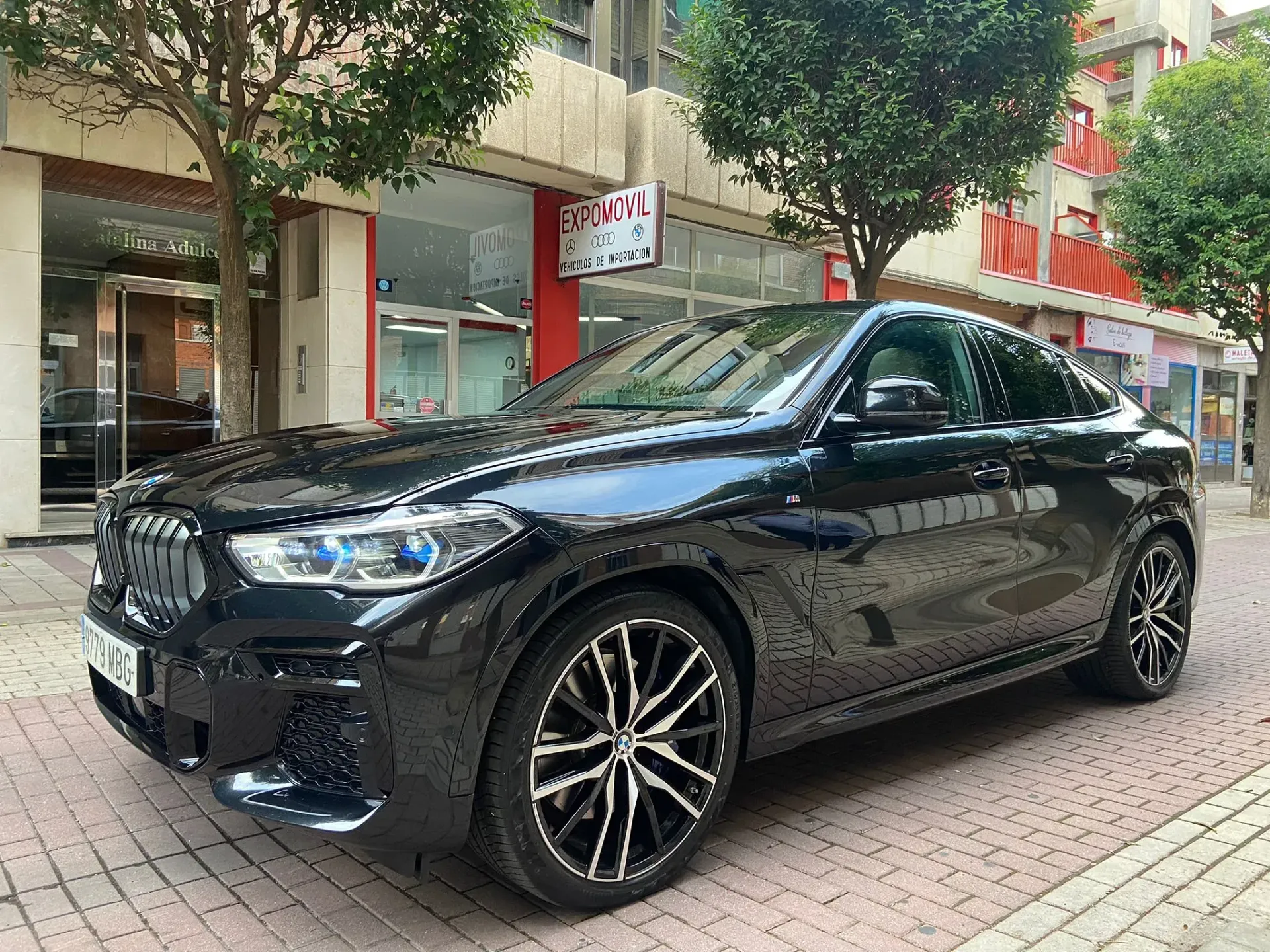 Un BMW X5 negro está estacionado en una acera de ladrillos frente a un edificio.