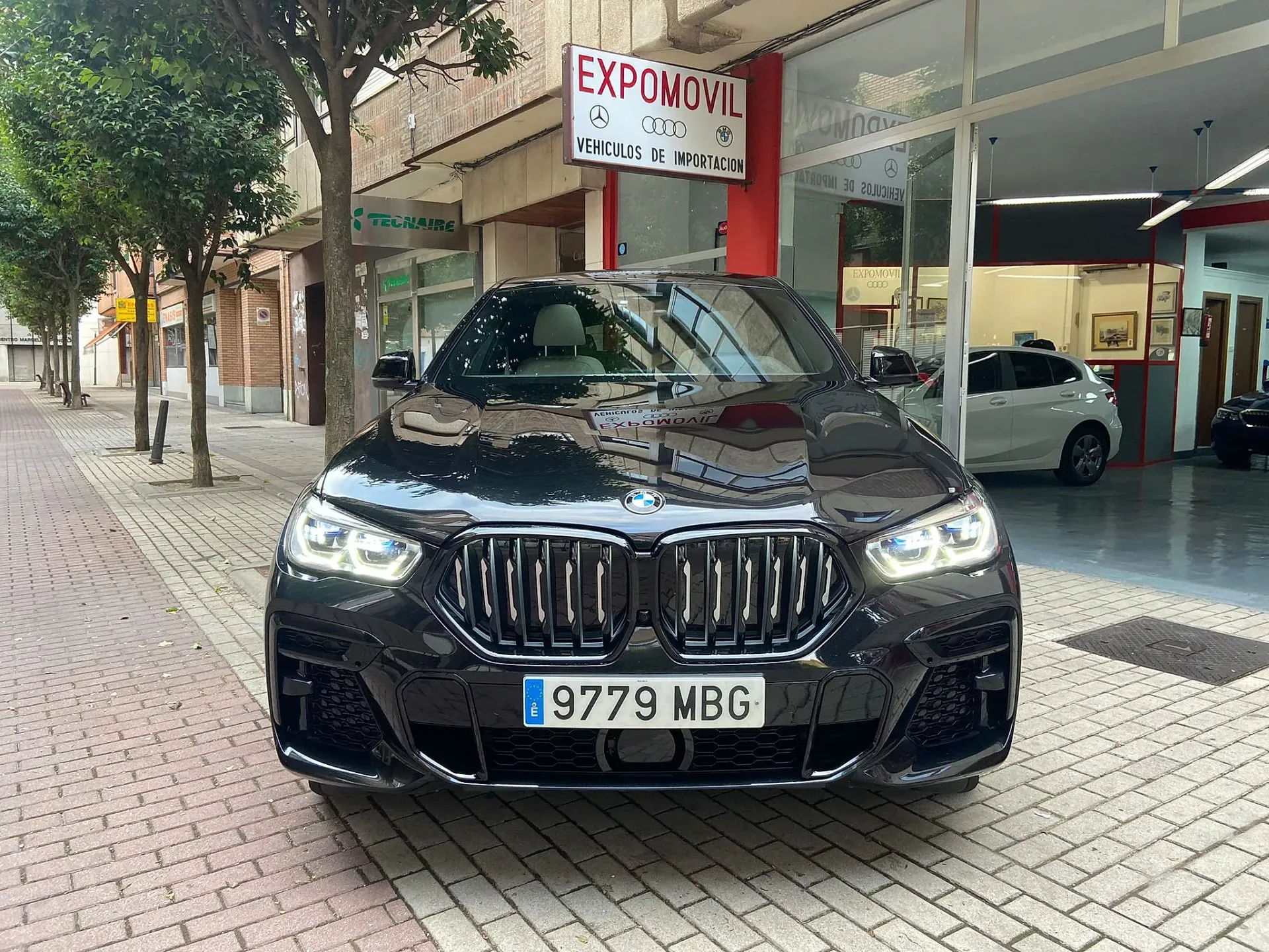 Un coche negro está estacionado en una acera de ladrillos frente a un concesionario de automóviles.