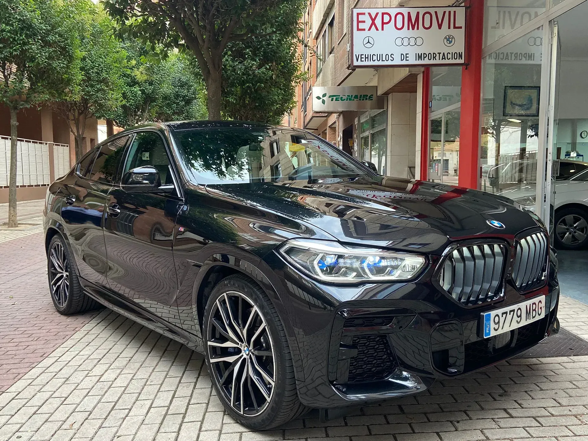 Un BMW X6 negro está estacionado frente a un concesionario de automóviles.