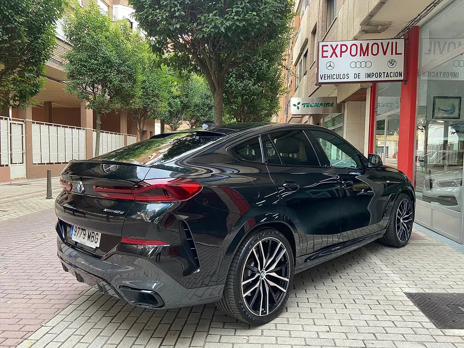 Un BMW X6 negro está estacionado frente a un concesionario de automóviles.