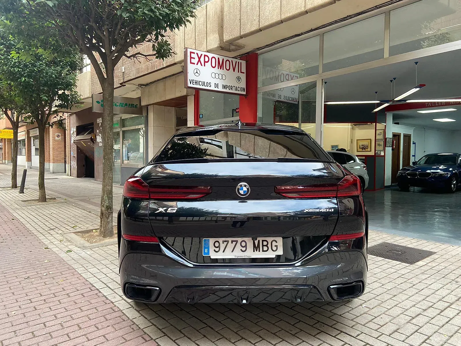 Un BMW X6 negro está estacionado frente a un concesionario de automóviles.