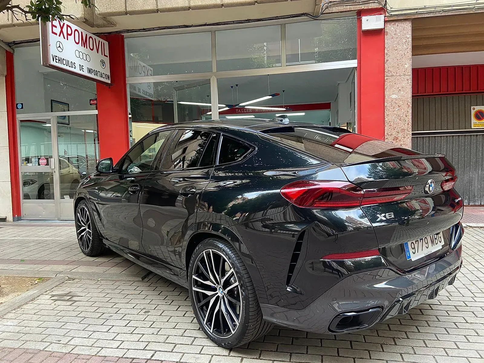 Un BMW X6 negro está estacionado frente a un concesionario de automóviles.