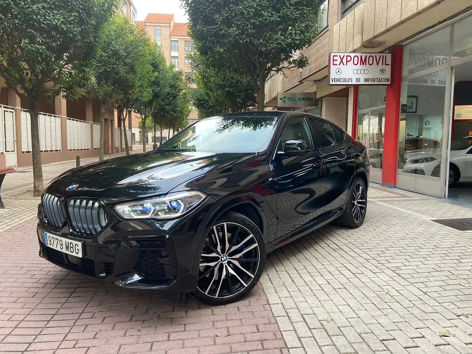 Un BMW X6 negro está estacionado frente a un concesionario de automóviles.